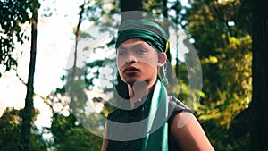 An Asian man in a green bandana and green clothes smiling while looking for someone in the forest