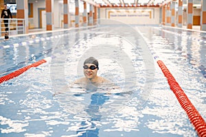 Asian man in hat and goggles swimming in swimming pool photo