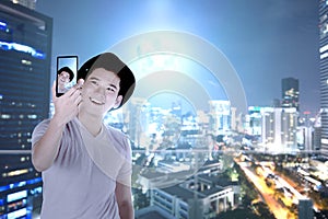 Asian man in hat making selfie using the camera phone with skyscrapers background