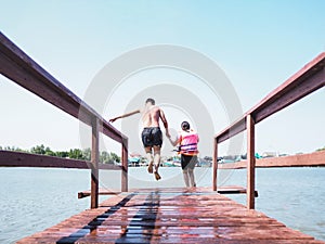 Asian man and his sister jumping off wooden bridge