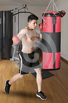 Asian man hitting a punching bag in gym center