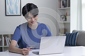 Asian man holding credit card and using laptop computer.Businessman working at home.Online shopping, e-commerce, internet banking.