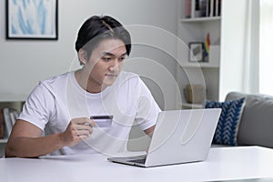 Asian man holding credit card and using laptop computer. Businessman working at home.Online shopping, e-commerce, internet banking