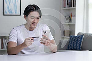 Asian man holding credit card and using smartphone. Businessman working at home. Online shopping, e-commerce, internet banking.