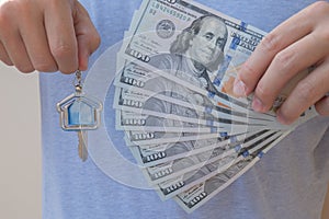 Asian man holding one hundred dollar bills and home shape key chain. Property investment and mortgage finance concept