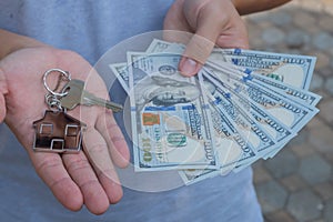 Asian man holding one hundred dollar bills and home shape key chain. Property investment and mortgage finance concept