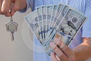 Asian man holding one hundred dollar bills and home shape key chain. Property investment and mortgage finance concept