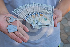 Asian man holding one hundred dollar bills and home shape key chain. Property investment and mortgage finance concept