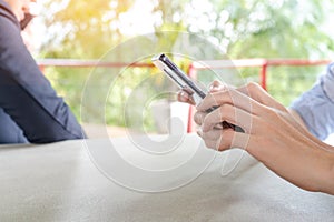 Asian man holding a phone, using smartphone while his business partner talking on a phone in background