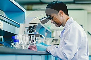 Asian man lab technician in protective glasses and gloves sits next to a microscope in laboratory