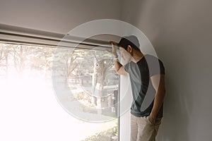 Asian man leaning against a wall, gazes out the window