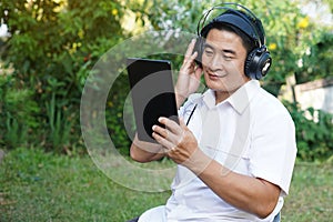 Asian man listen to music from headphone, holds digital smart tablet.