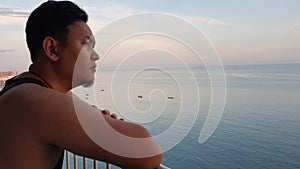 Asian man looking to the ocean from balcony at dawn or sunset, thinking contemplating
