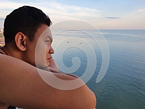 Asian man looking to the ocean from balcony at dawn or sunset, thinking gesture
