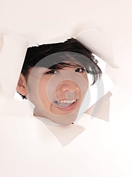 Asian man looking trough hole in paper.