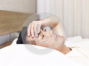 Asian man lying on bed hand on forehead