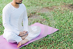 Asian man meditating on green grass in the park, calm and focused, health and yoga meditation concept, with copy space