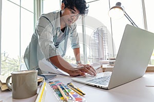 Asian man messy hair working in Architect or Interior Designer study about building design with laptop and drawing paper, Building