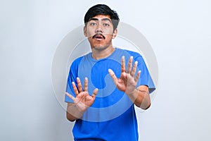 Asian man moving away hands palms showing refusal and denial with afraid and disgusting expression. Stop and forbidden
