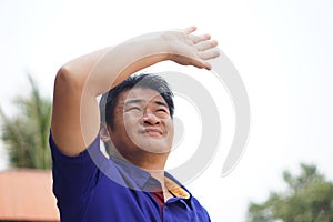 Asian man is outdoor, face up to sky, hand over his head, feel hot and unwell.