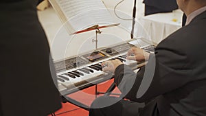 Asian Man playing electronic musical keyboard synthesizer by hands on white and black keys on stage performance