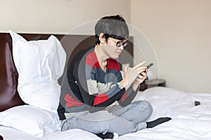 Asian man playing phone on bed