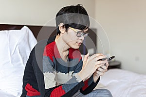 Asian man playing phone on bed