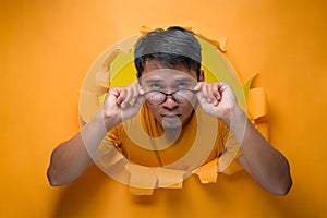 Asian man poses over torn paper hole with eyeglasses seriously looking at the camera