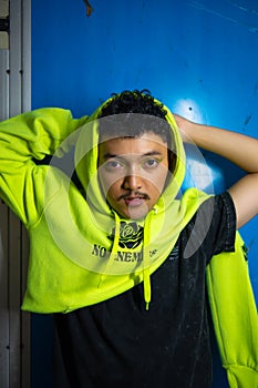 an Asian man posing stylishly while wearing a green hoodie in front of a locker