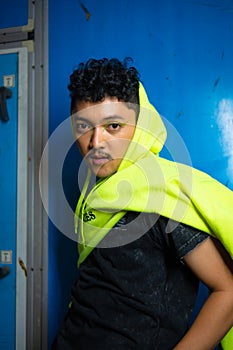 an Asian man posing stylishly while wearing a green hoodie in front of a locker