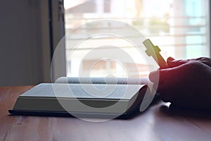 Asian man praying while holding wooden cross in front of the bible