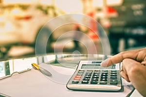 Asian man pressing calculator for business finance on car showroom blurry background.for automotive or transportation