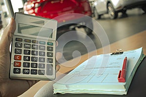 Asian man pressing calculator for business finance on car showroom blurry background.for automotive or transportation