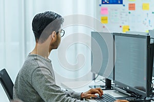 Asian man prompt engineer develop coding app with software data sitting in front of computer monitor at office