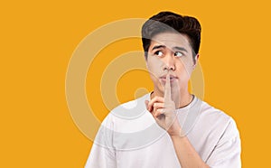 Asian man puting finger on his lips, making hush sign