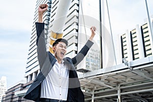 Asian man raise hand with happiness in city feels glad to get new job. Young businessman feeling happy and free after he knew the