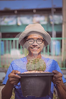 Asian man raising melocactus pot and toothy smiling with happiness