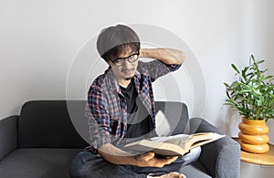 Asian man rubbing eye with tired expression after long period reading book.