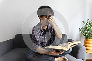 Asian man rubbing eye with tired expression after long period reading book.