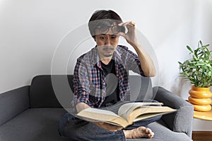 Asian man rubbing eye with tired expression after long period reading book.