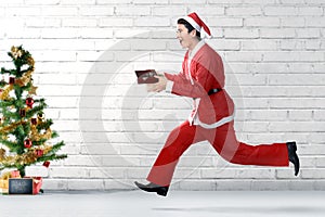 Asian man in Santa costume running while holding the gift box with a Christmas tree