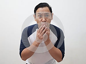 Asian man shocked and worried to see something bad, covering his mouth with hands and big eyes open, over grey