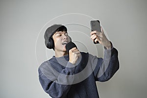 Asian man singing listening to music on smartphone wearing headphones.