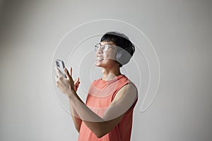 Asian man singing listening to music on smartphone wearing headphones.