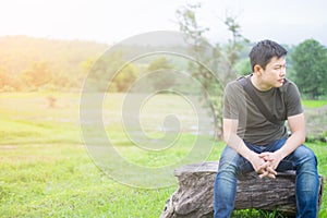 Asian Man, sitting alone on the bench. The background green meadow and mountain.