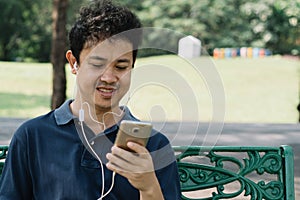 Asian man sitting on the bench with earphone in the garden