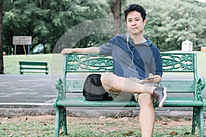 Asian man sitting on the bench with earphone in the garden