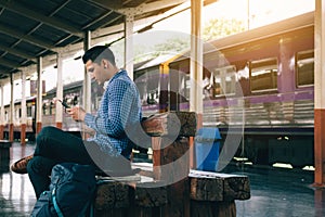 Asian man sitting on bench and using smartphone with waiting train.