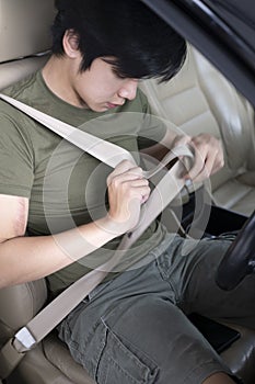 Asian man sitting in car and fastening seat belt.