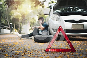 Asian man sitting beside car and using mobile phone calling for assistance after a car breakdown on street. Concept of vehicle